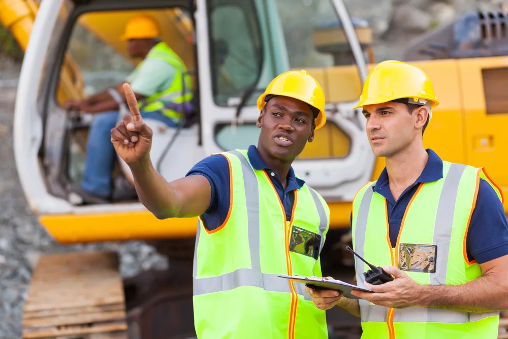Site supervisor in a high visibility vest directing work beside an excavator